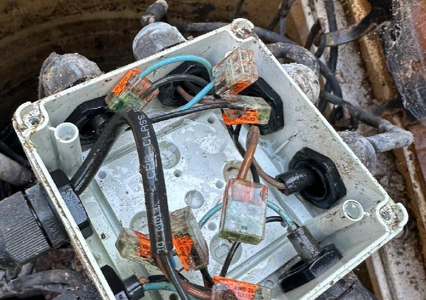 Open junction box with orange and white connectors beside pump chamber cables