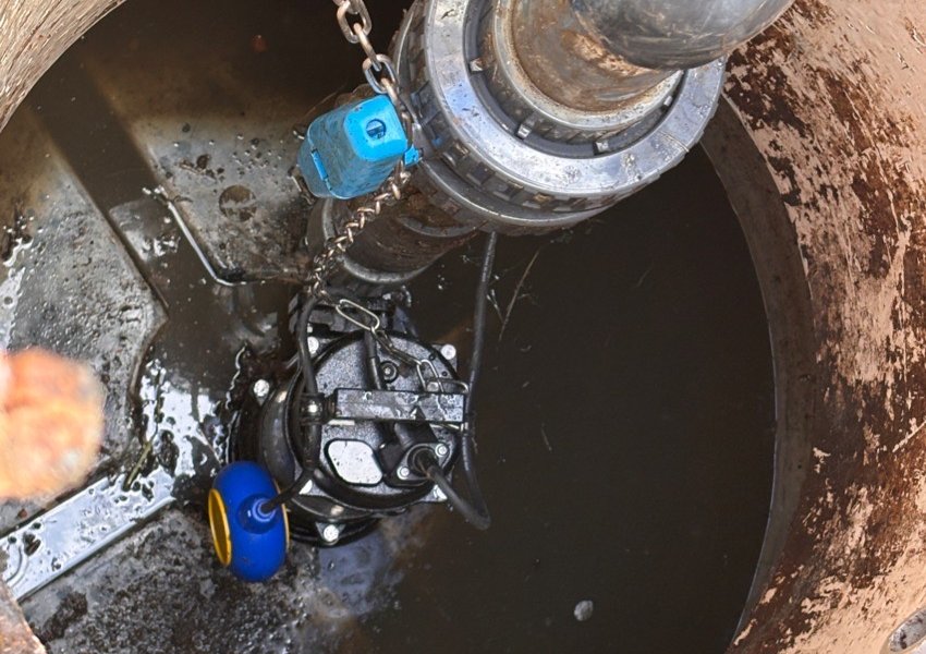Engineer lowering a submersible pump on its chain into a pump chamber